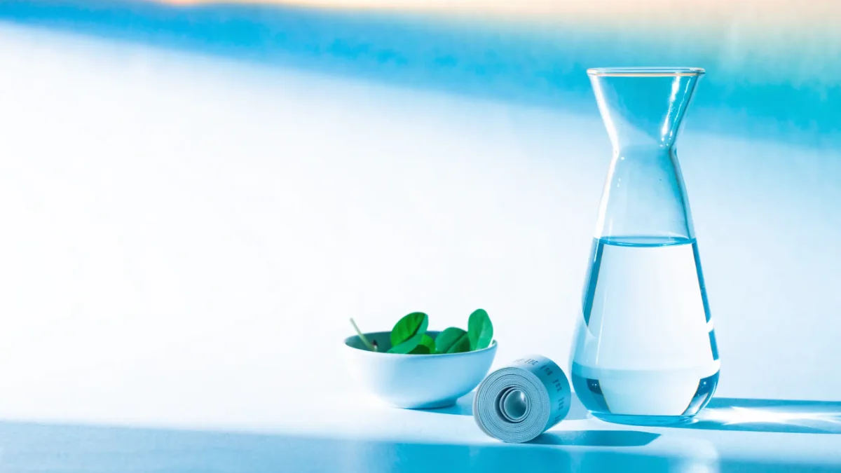 Wasserkaraffe, Maßband und Schale mit frischen Blättern