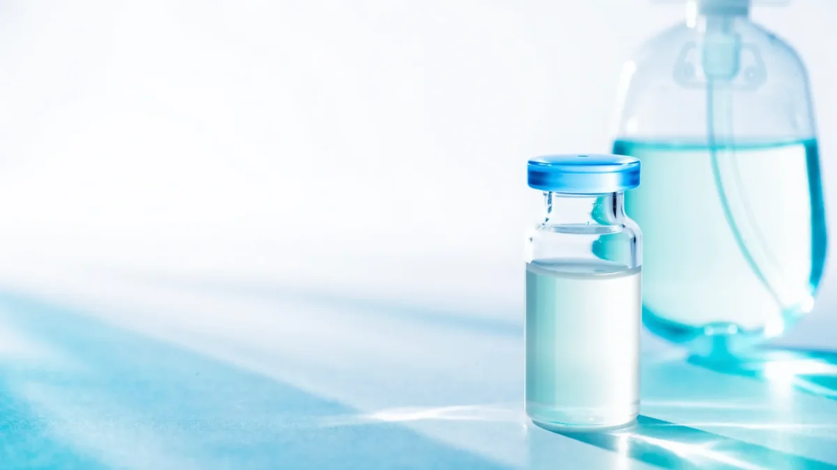 Glasfläschchen mit milchig weißer Lösung vor einem Infusionsbeutel